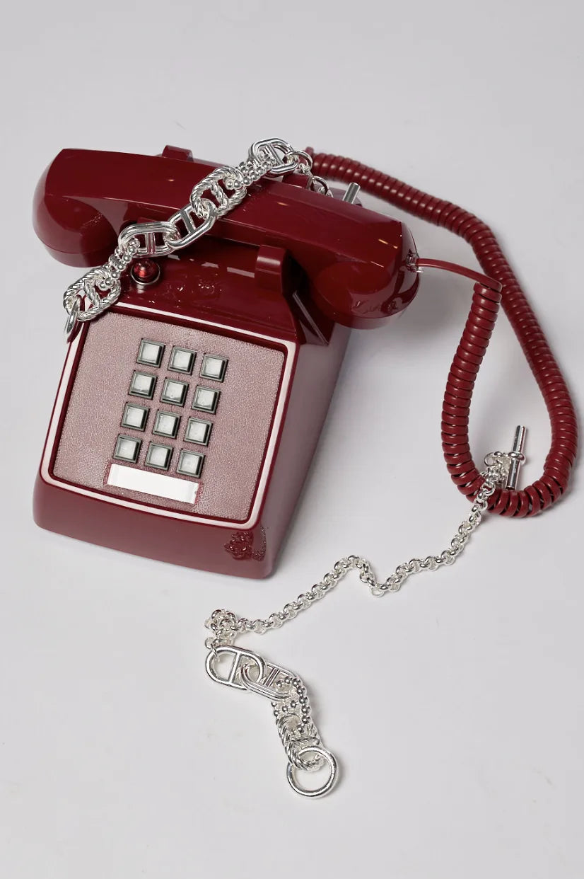 A vintage burgundy push-button telephone with a silver chain draped over it on a taupe background