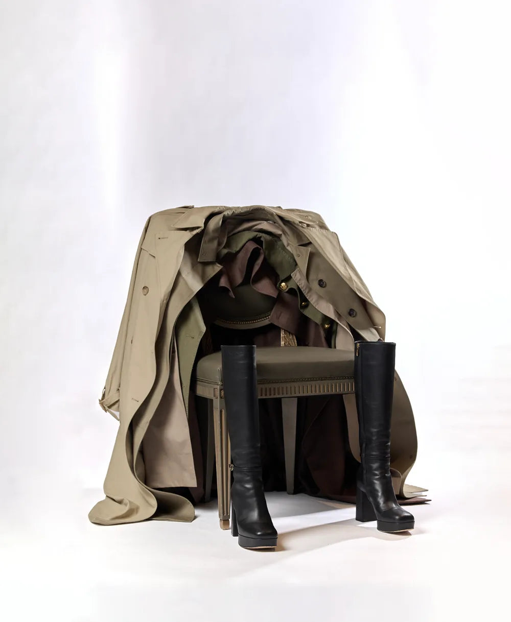 Designer trench coat draped over a chair with knee-high boots