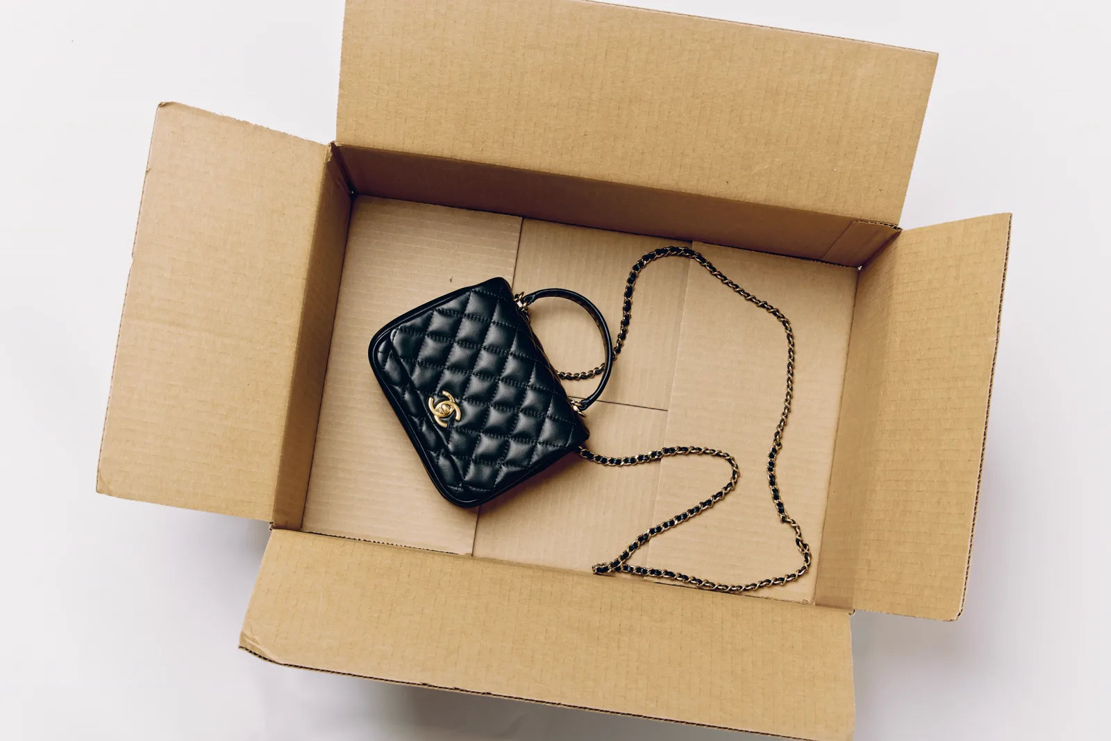 A small black quilted Chanel bag inside an open cardboard shipping box