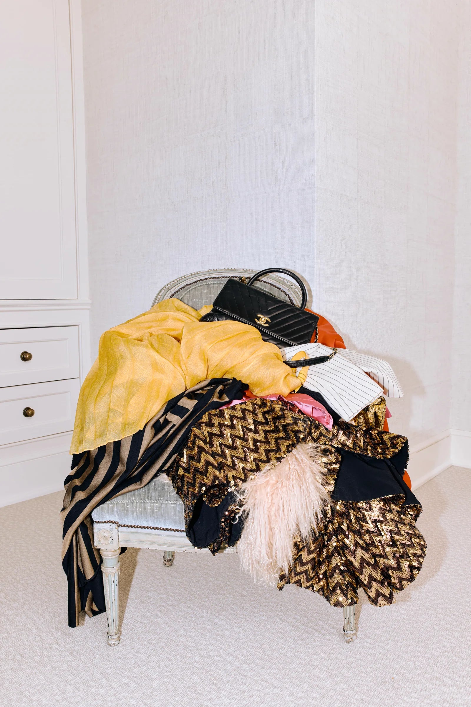 Pile of luxury garments and a Chanel bag draped over a small chair